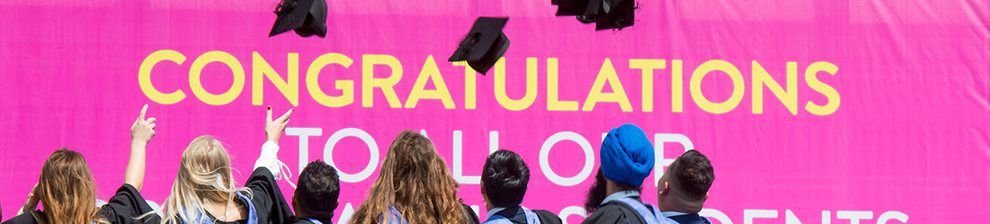 A group of graduates on the seafront promenade throwing their mortar boards in the air