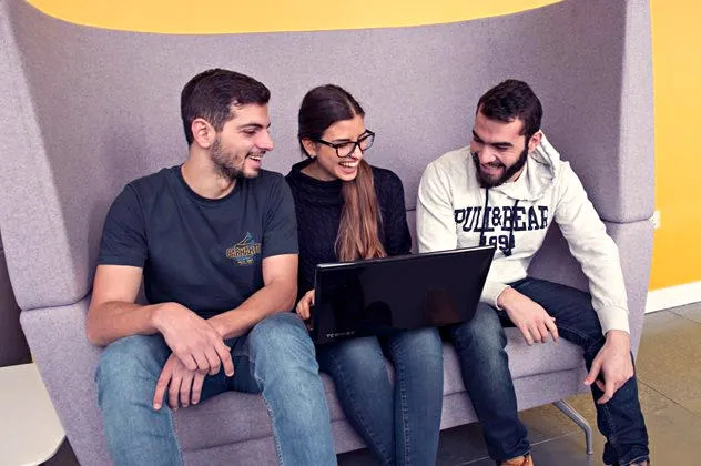 Three students sitting in a booth looking at a laptop