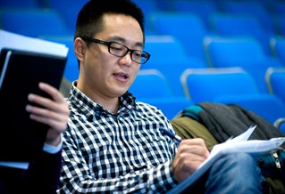 A student in a lecture hall making notes on paper