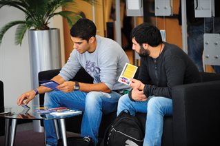 Two international students looking at leaflets sat on a sofa