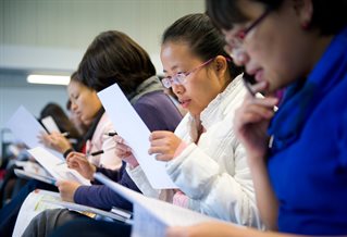 A line of students sitting down and reading a sheet of paper