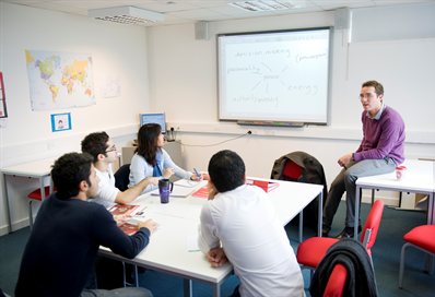 Students around a table listening to a lecturer