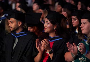 Graduating student sitting in the crowd and clapping at graduation ceremony