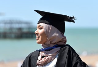 Student on graduation wearing a gown and cap infront of the sea