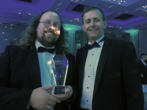 Two men in evening dress, one holding a glass award