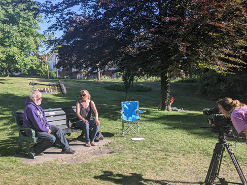 Two people chatting on a park bench while being filmed