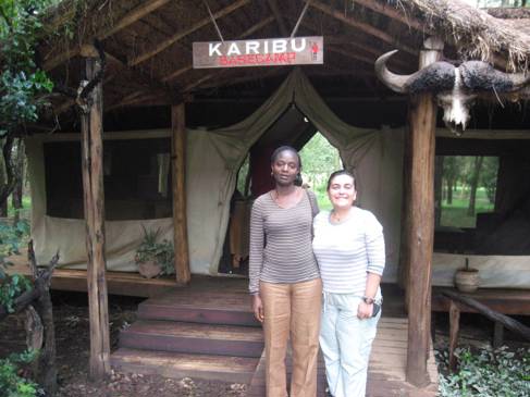 Two women standing outside a small wooden building, with a sign: KARIBU basecamp