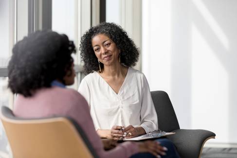 Two black women facing each other in chairs at a counselling session