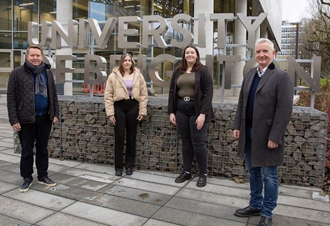 Four people standing in front of the University of Brighton sign