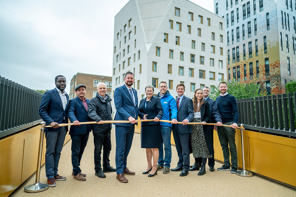 Ten people standing behind a ribbon, about to be cut, on a bridge