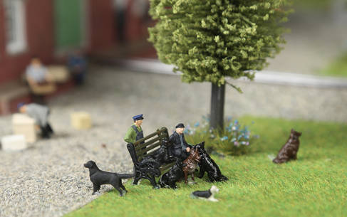 Diorama of people sitting outside on a bench surrounded by dogs