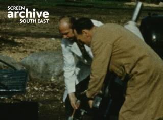 Grainy 50s colour film shot of two male engineers carrying equipment at Stonehenge. Courtesy Screen Archive South East and the Phillips family.