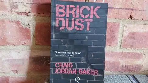 A book titled 'Book Dust' leans against a brick wall