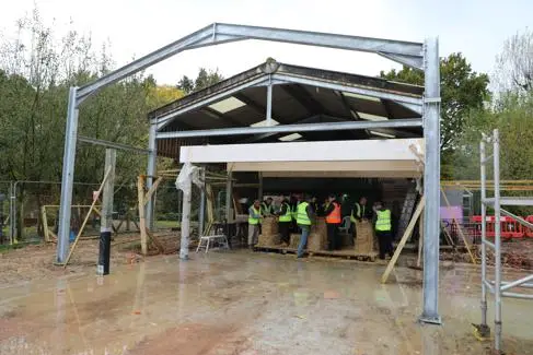 A building structure, in which people in high vis jackets make straw bales