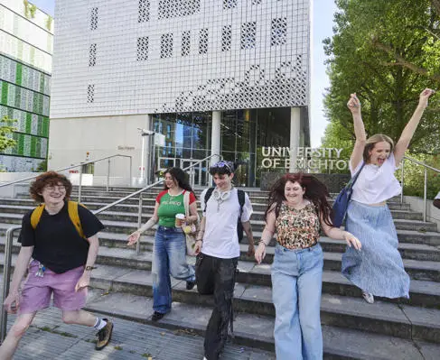 A group of university students smile in front of a University of Brighton building