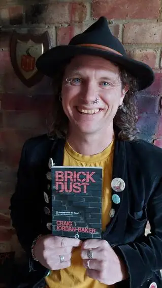 A man wearing a hat smiles as he holds open a book