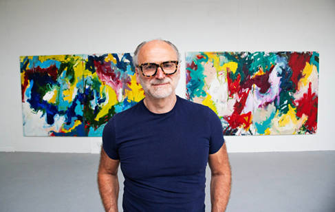 A mature student wearing glasses, standing in front of two colourful abstract paintings