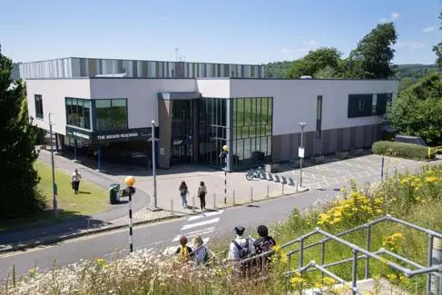 A modern building surrounded by students walking around it. A blue, clear sky in the background.