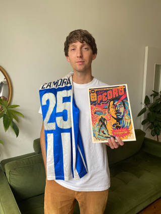 A young man holding a football brochure he has designed and wearing a Brighton & Hove Albion football scarf