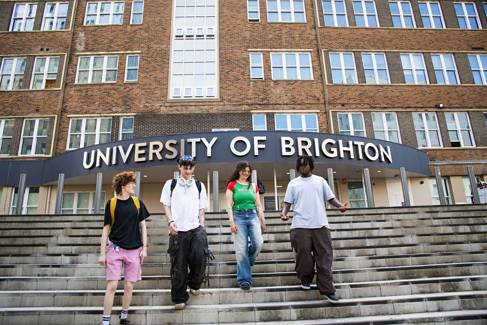 Four young teens walking down concrete steps in front of a large building that reads 'The University of Brighton'