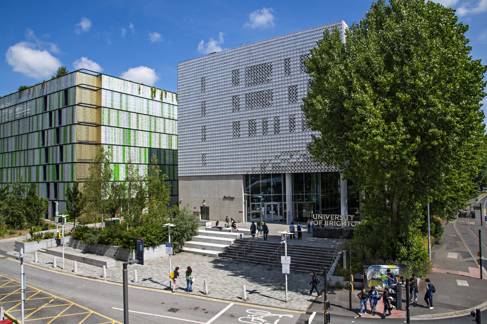 Modern building surrounded by students on a summer's day with a sign reading 'the University of Brighton'