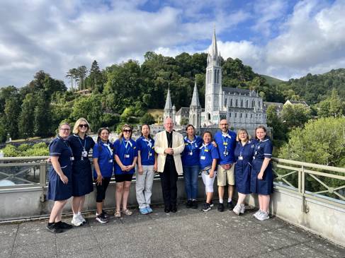 Nursing students wearing blue smile to have their picture taken with a Cardinal in front of a church