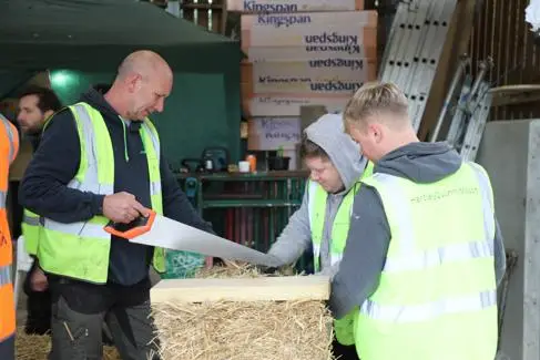 One man saws a straw bale. Two men face him