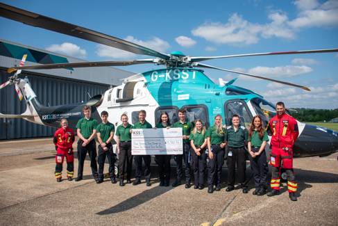 Paramedic students and air ambulance staff stood in front of a blue helicopter, holding a giant cheque