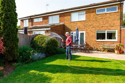 An older man watering his back garden on a sunny day