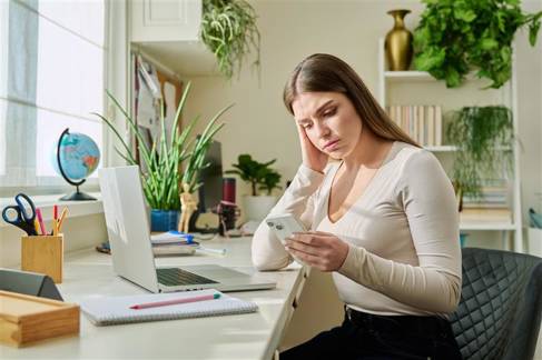 Serious young woman sitting at home reading texting on smartphone