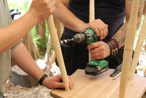 Two pairs of hands hold a chair as it's being built.