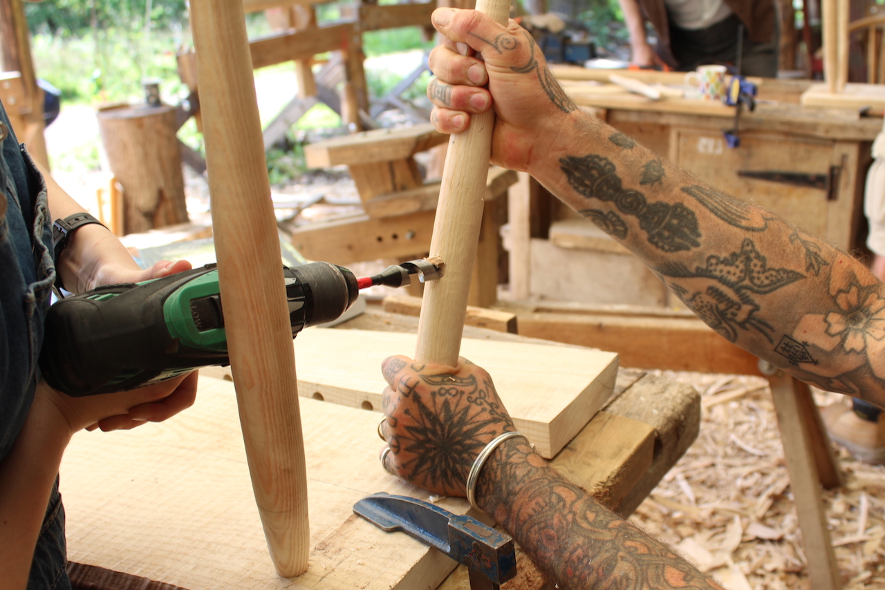 A pair of tattooed arms hold a chair as it's being built