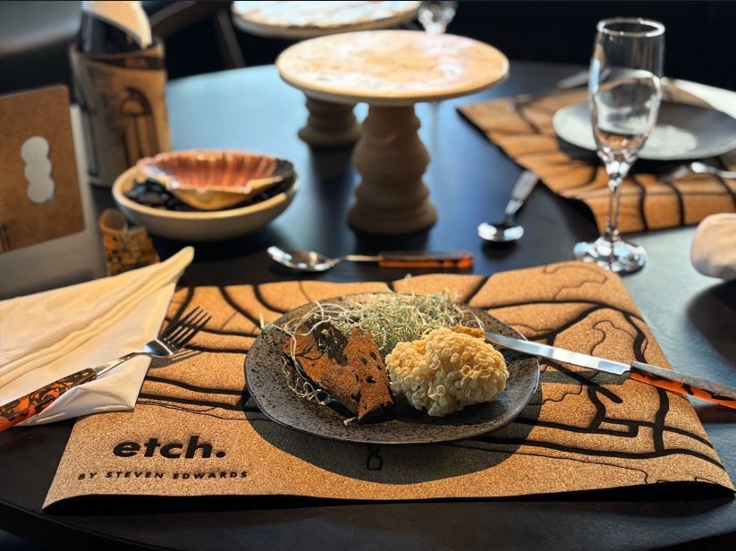 Dining table covered with mats, cutlery, wine holders, and cake stands - all made of cork