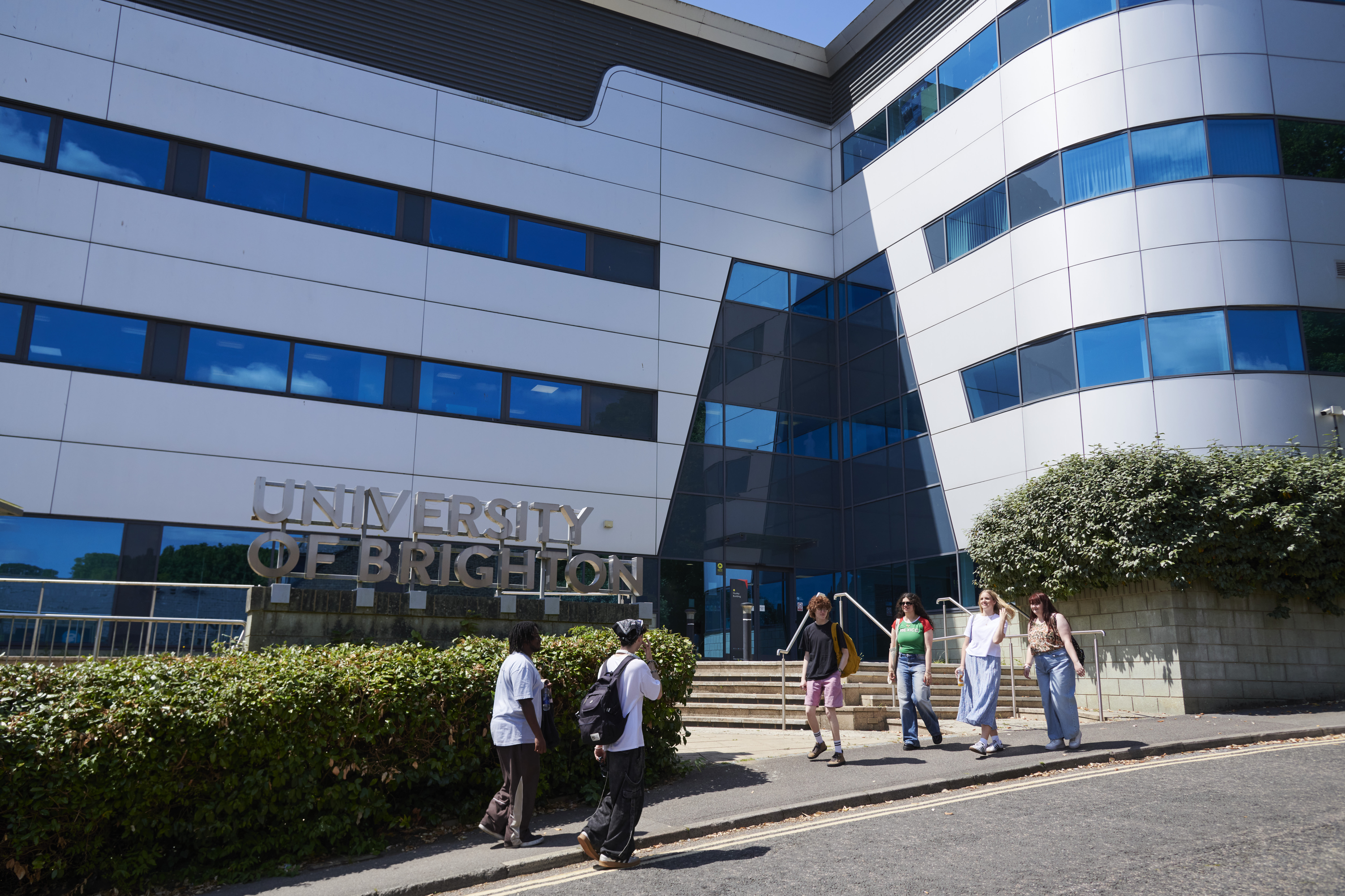 Modern white building with students stood in front of it.