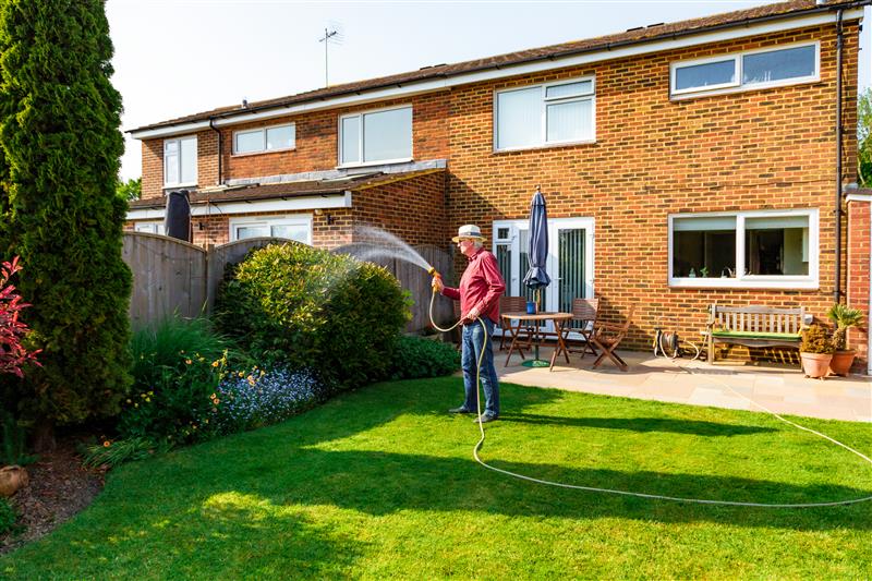 Picture of a man watering his back garden on a sunny day