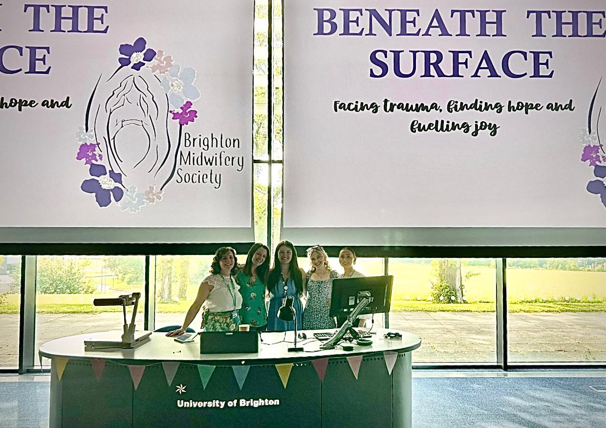 Student midwives post at conference in front of a sign that reads ' Beneath the Surface