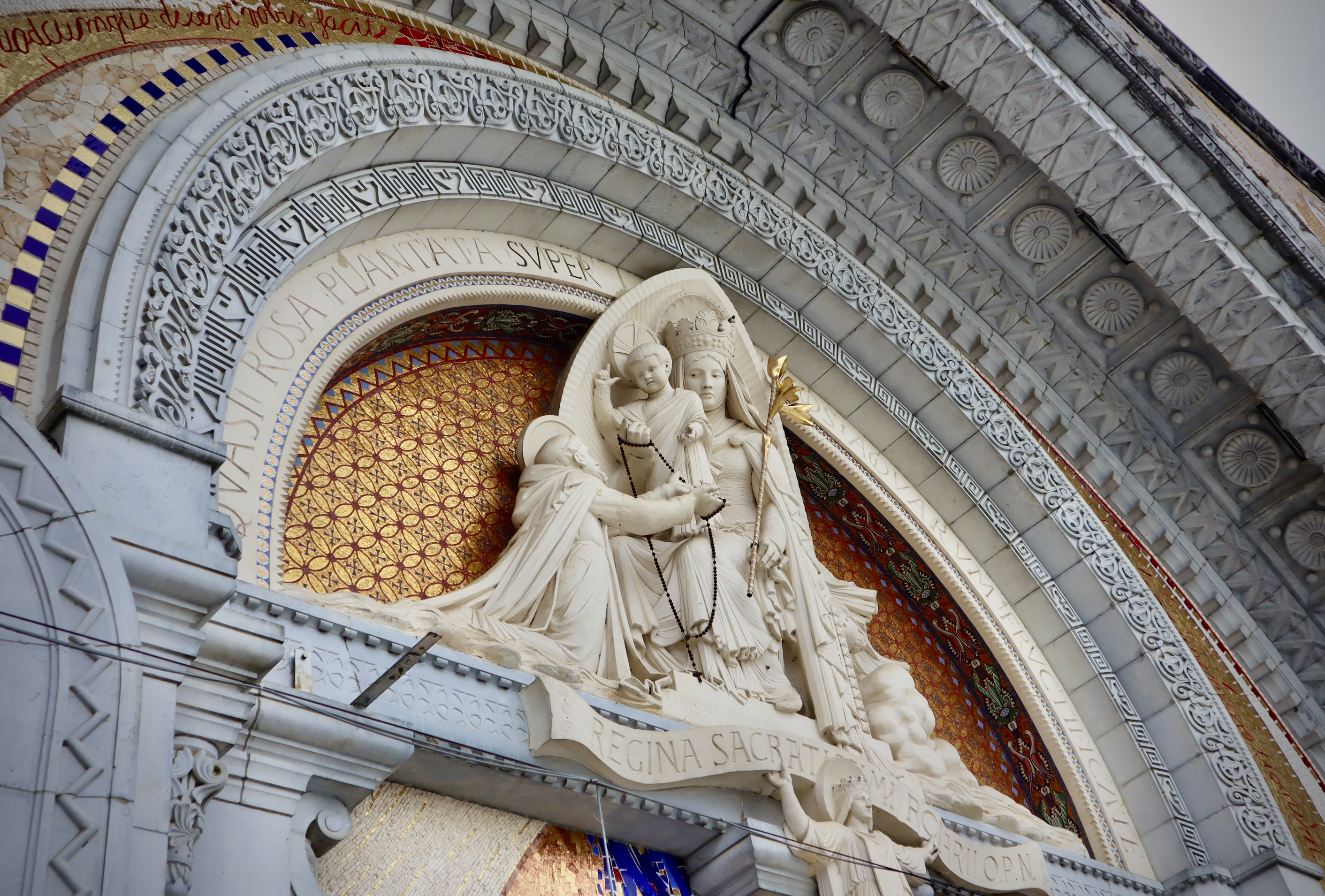 The outside of a church, covered in colourful and a marble statue depicting a saint holding a baby