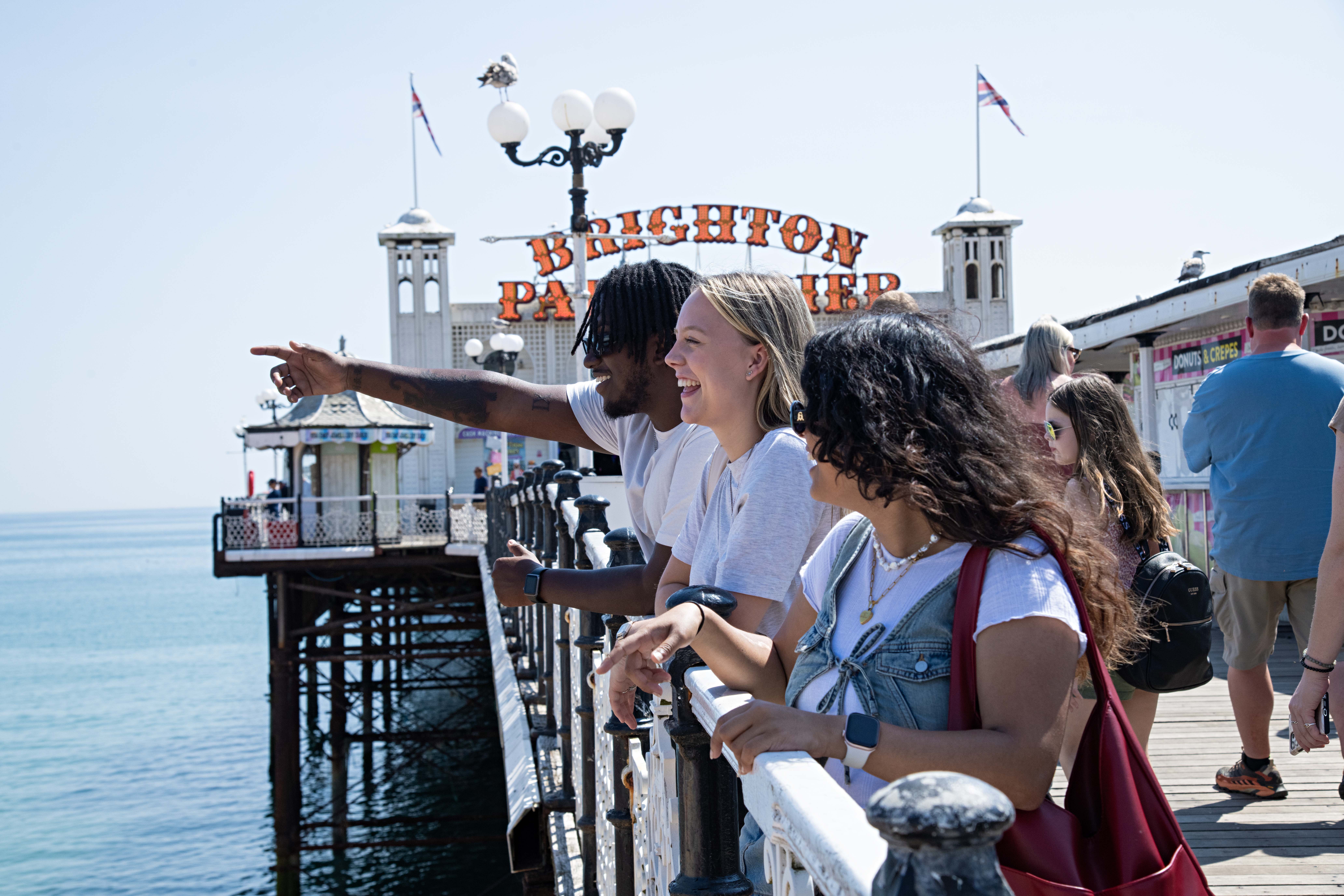 Three young teens stood on Brighton pier on a sunny day looking out to sea