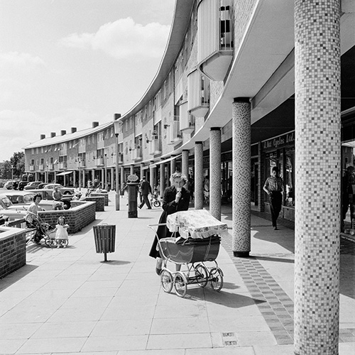 A black and white photo of a woman with a pram in an urban environment
