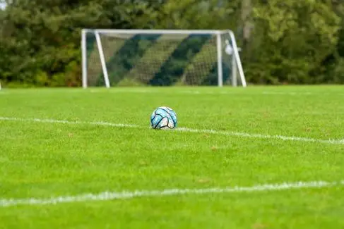 A football sits alone in a football field, in front of an empty goal