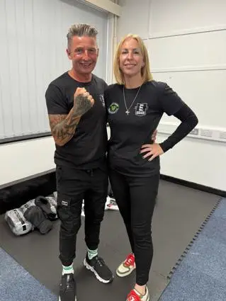 A man and a woman in gym clothes smile at the camera