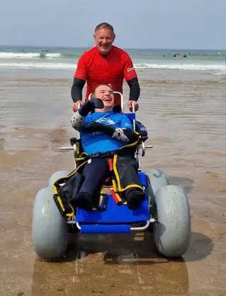 A man pushes someone in a beach friendly wheelchair