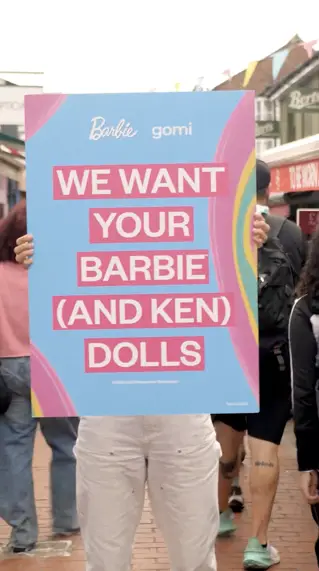 A pair of legs holding up a sign saying we want your barbie dolls
