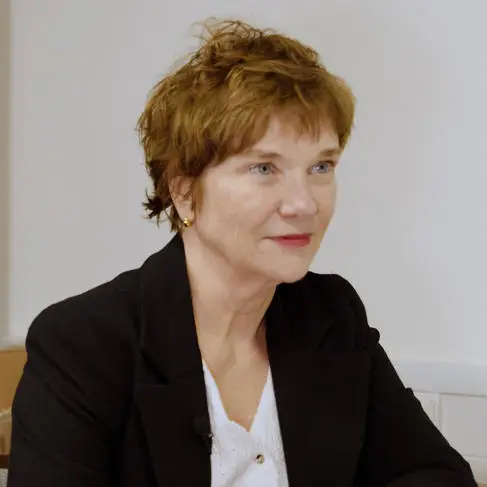 A portrait of a white woman, with short brown hair and wearing a black suit. Anne Daguerre