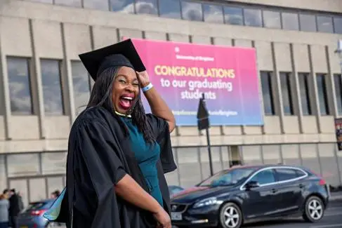A woman dressed in graduation robes smiles and poses for the camera