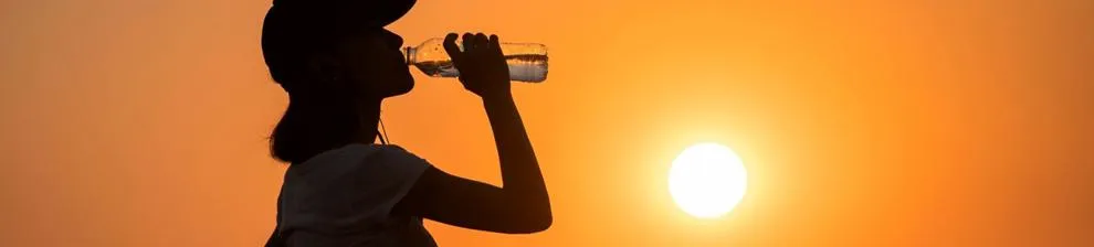 A woman drinks water with the sun glaring in the background
