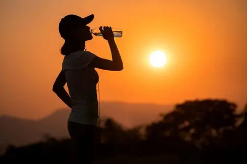 A woman drinks water with the sun glaring in the background