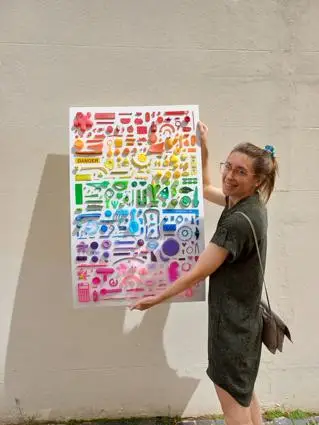 A woman holds a piece of art, made out of colourful plastic pieces