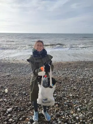 A woman holds two bags on the beach, collecting plastic