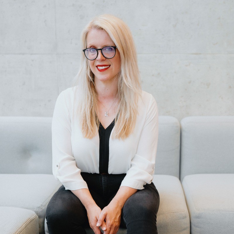 A woman sits on a grey sofa and smiles